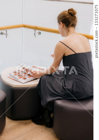 woman in library is reading book sitting on wide chair. lady in black dress flips through pages.  133271075