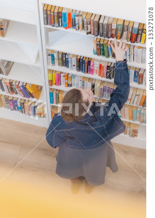 top view of woman at shelves in the library with laptop in her hands, choosing a book. top view of woman at shelves in the library with laptop in her hands, choosing a book. 133271078