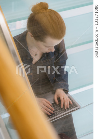 young woman is sitting on glass staircase with laptop in front of her and working. business person. young woman is sitting on glass staircase with laptop in front of her and working. business person. 133271080