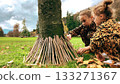 Children building a toy stick house around a tree in a park 133271367
