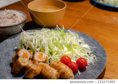 A home-style dinner of pork wrapped in vegetables, shredded cabbage, mixed grain rice, and miso soup 133271405