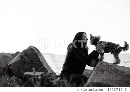 Black and white photo of a young woman with long hair gently touching her small Yorkshire terrier doggy. Emotional connection of human and lovable pet 133271842