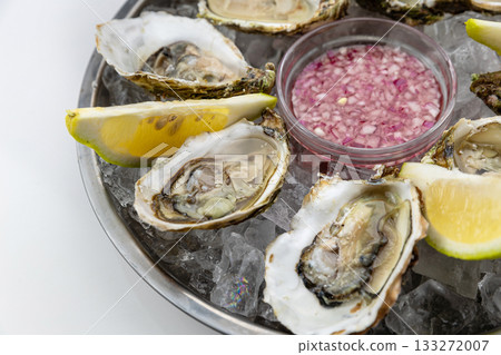 Closeup of fresh oysters on ice with lemon wedges and mignonette, seafood detail Closeup of fresh oysters on ice with lemon wedges and mignonette, seafood detail 133272007