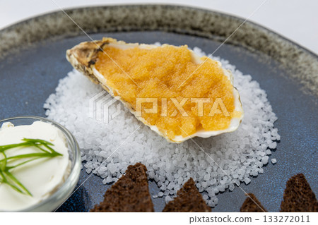 Closeup oyster shell with orange caviar on sea salt, with rye toasts and sour cream Closeup oyster shell with orange caviar on sea salt, with rye toasts and sour cream 133272011