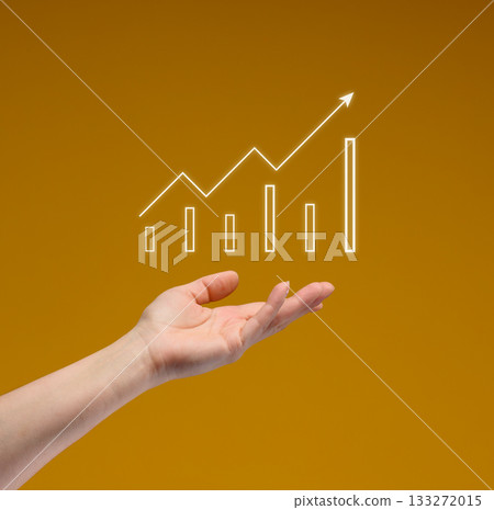 A woman's hand holds a glowing digital graph with an upward trend, a bar chart, and a growth line on a yellow background. A woman's hand holds a glowing digital graph with an upward trend, a bar chart, and a growth line on a yellow background. 133272015