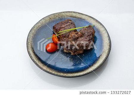 Seared beef steak on blue ceramic plate with cherry tomatoes, minimal gourmet plating 133272027