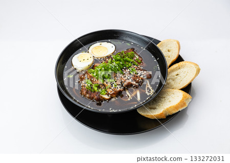 Black bowl of soy ramen with sliced pork, egg, scallions and sesame, isolated on white 133272031