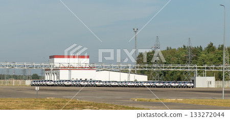 A vast outdoor storage lot at an automotive factory is filled with rows of brand-new, white cars 133272044