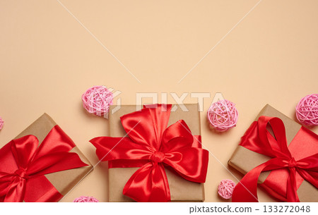 Gifts wrapped in red satin ribbon with a bow on a beige background Gifts wrapped in red satin ribbon with a bow on a beige background 133272048