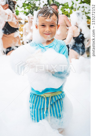 Happy caucasian child boy smiles at foam party on the beach in summer on vacation Happy caucasian child boy smiles at foam party on the beach in summer on vacation 133272152