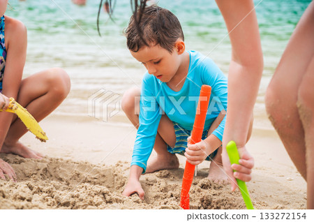 Caucasian child boy plays on beach and builds a sand castle with friends in summer by the sea on vacation Caucasian child boy plays on beach and builds a sand castle with friends in summer by the sea on vacation 133272154