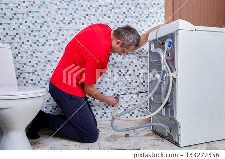 Service technician manually connects water supply hose to threaded water pipe extending from wall for washing machine water intake. Service technician manually connects water supply hose to threaded water pipe extending from wall for washing machine water intake. 133272356