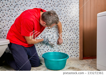 Plumber removes steel plug from water inlet pipe using special wrench and prepares connection point for washing machine installation. 133272361
