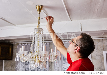Dismantling operation captures electrician removing entire crystal chandelier from ceiling in rural house, 133272368