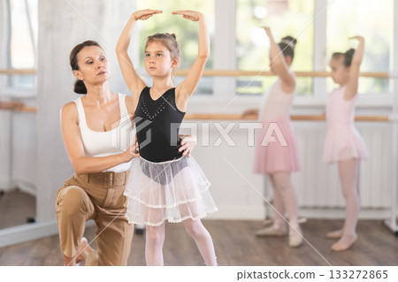 In studio, mentor corrects girls arm and leg, teaches correct dynamics and execution of movements In studio, mentor corrects girls arm and leg, teaches correct dynamics and execution of movements 133272865