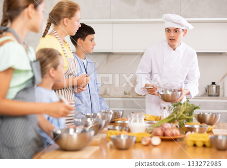 Group of teenagers and friendly chef cook cooking in modern kitchen. Learn to beat raw eggs 133272985