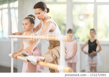 Woman teacher helps girl stretch at barre Woman teacher helps girl stretch at barre 133272991