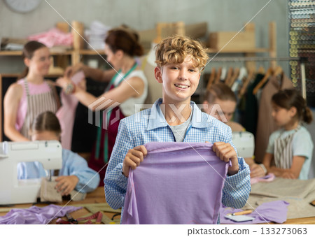 Teenage boy happily shows off a t-shirt he sewed with his own hands on sewing machine Teenage boy happily shows off a t-shirt he sewed with his own hands on sewing machine 133273063