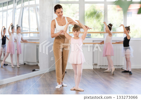 Ballet lesson for little girls - choreography teacher shows little ballerinas how to get into different poses correctly in sturio 133273066
