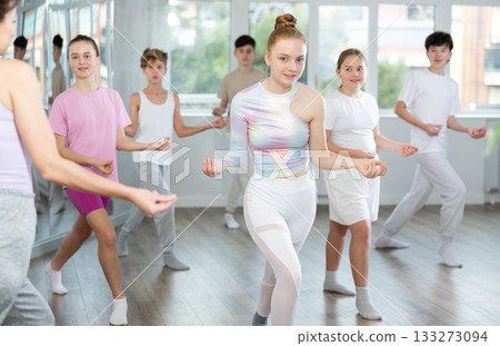 Female girl student repeats movements of unrecognizable teacher during group modern dance class. Female girl student repeats movements of unrecognizable teacher during group modern dance class. 133273094