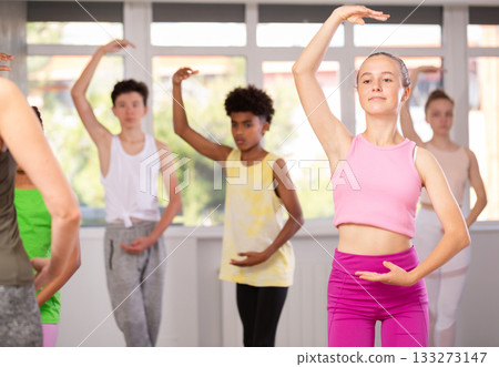 Positive teenage girl practicing ballet positions standing in row with others Positive teenage girl practicing ballet positions standing in row with others 133273147