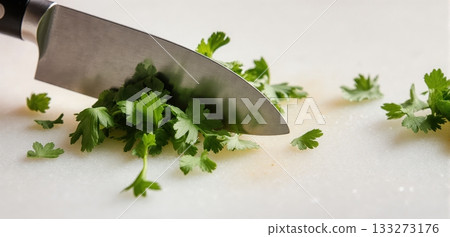 Close-up of a knife finely chopping fresh coriander on a clean cutting board Close-up of a knife finely chopping fresh coriander on a clean cutting board 133273176