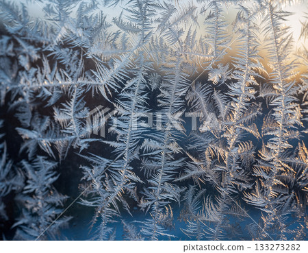 A close-up of delicate, beautiful frost crystals resembling fern leaves on a window pane on a winter morning A close-up of delicate, beautiful frost crystals resembling fern leaves on a window pane on a winter morning 133273282
