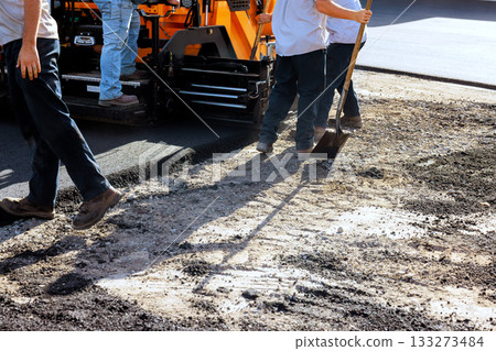 Workers perform asphalt paving on construction site in busy urban area 133273484