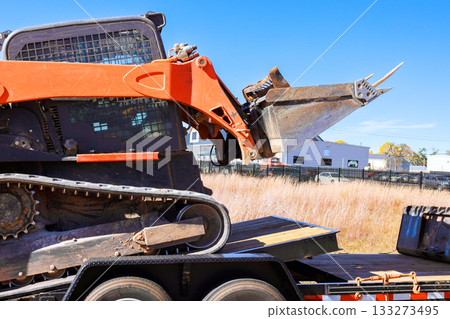 Skid steer machinery loader ready for transport on flatbed trailer 133273495