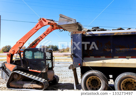 Bobcat machinery moves soil into dump truck during construction work 133273497
