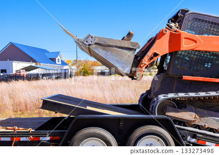 Excavator unloading materials on flatbed trailer at construction site 133273498