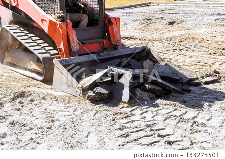 Construction machine operates on site, moving broken concrete debris during renovation work 133273501