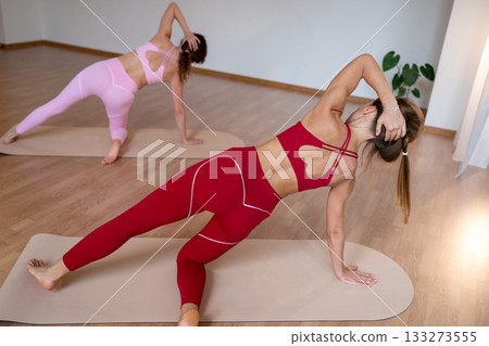 Active women execute coordinated side planks with trainer guidance in welllit studio setting 133273555