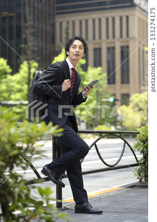 一位三十多歲的商人戴著耳機，手裡拿著一支智慧型手機。 133274175