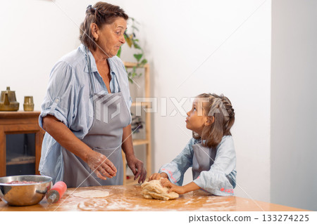 Girl baking with grandmother kneading dough on 133274225