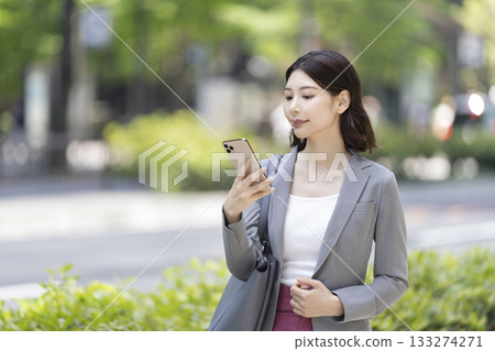 一位女商人外出時正在查看智慧型手機螢幕。 133274271