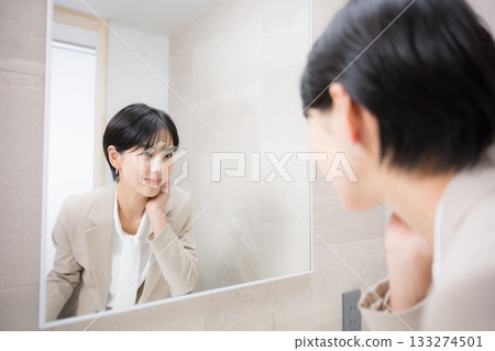 Beauty scene of a woman smiling in front of the mirror and fixing her makeup 133274501