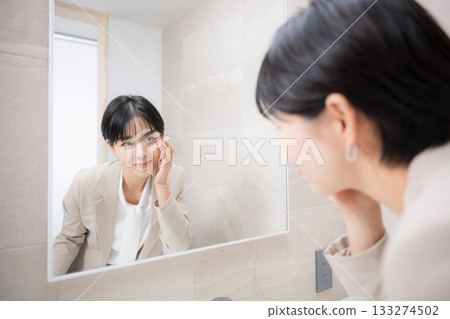 A woman smiling in front of the mirror, fixing her makeup, checking her contacts, etc. 133274502