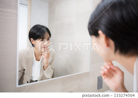 一位女士對著鏡子微笑，整理妝容，檢查嘴唇。 133274504