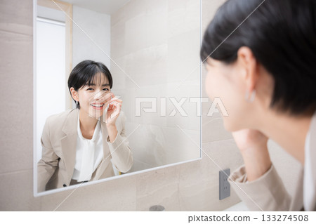 A woman checking her appearance after a meal in the bathroom, including checking her teeth 133274508