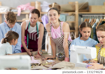 Sewing lesson - a group of teenage children learn to sew on sewing machine and cut fabric Sewing lesson - a group of teenage children learn to sew on sewing machine and cut fabric 133274629