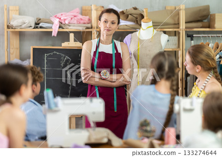 Woman teacher at blackboard conducts theoretical lesson for sewing school children students Woman teacher at blackboard conducts theoretical lesson for sewing school children students 133274644