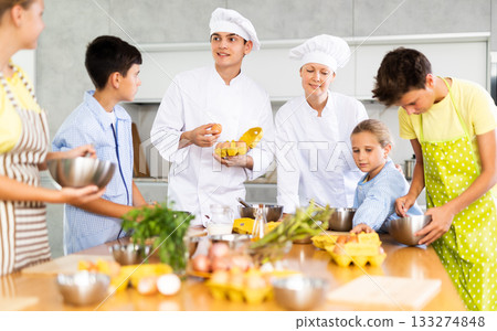Man and woman cooks, during culinary master class, tell children rules when preparing dough Man and woman cooks, during culinary master class, tell children rules when preparing dough 133274848