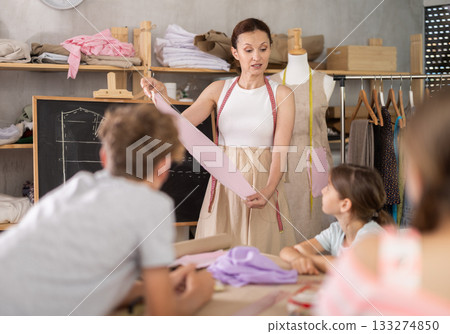 Female teacher at the blackboard explains to children how to make patterns and sew dress 133274850