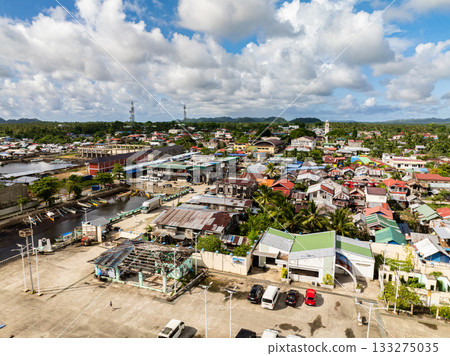 Busy town center with colorful houses, vehicles and palm trees set against mountains and blue sky. Del Carmen. Siargao, Philippines. 133275035