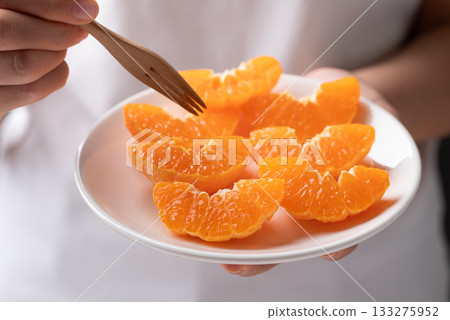 Fresh cut of Mandarin orange fruit on plate holding by hand ready to eating 133275952
