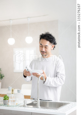 Housework scene of a man wiping dishes with a smile in a bright kitchen 133276287