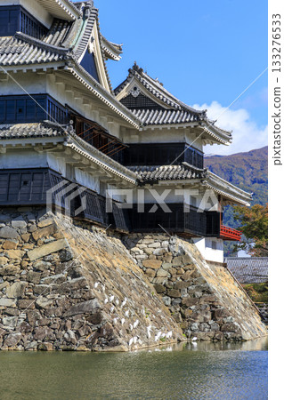 A tranquil autumn scene with the stone walls of Matsumoto Castle and white birds gathering on the water's surface 133276533