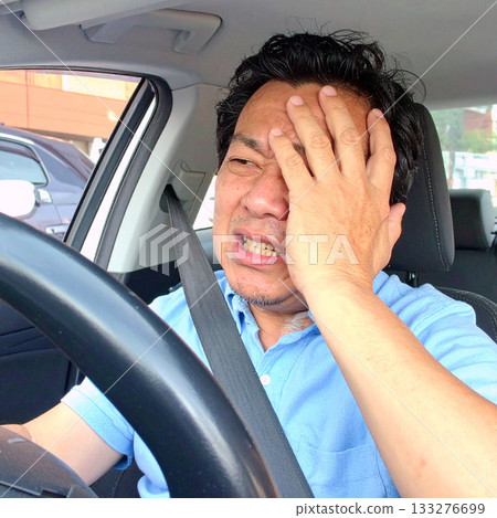 A middle-aged driver covers his face after crashing his car 133276699