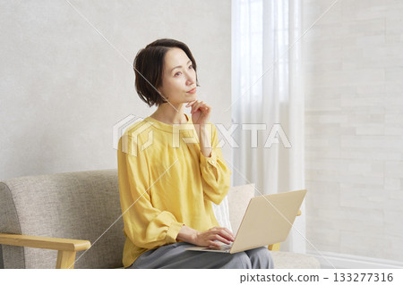 A woman using a computer in the living room thinking A woman using a computer in the living room thinking 133277316